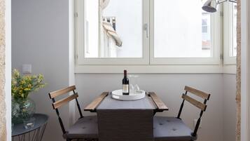 A small dining area with two wooden chairs, a table with a wine bottle and glass, and a vase with yellow flowers.
