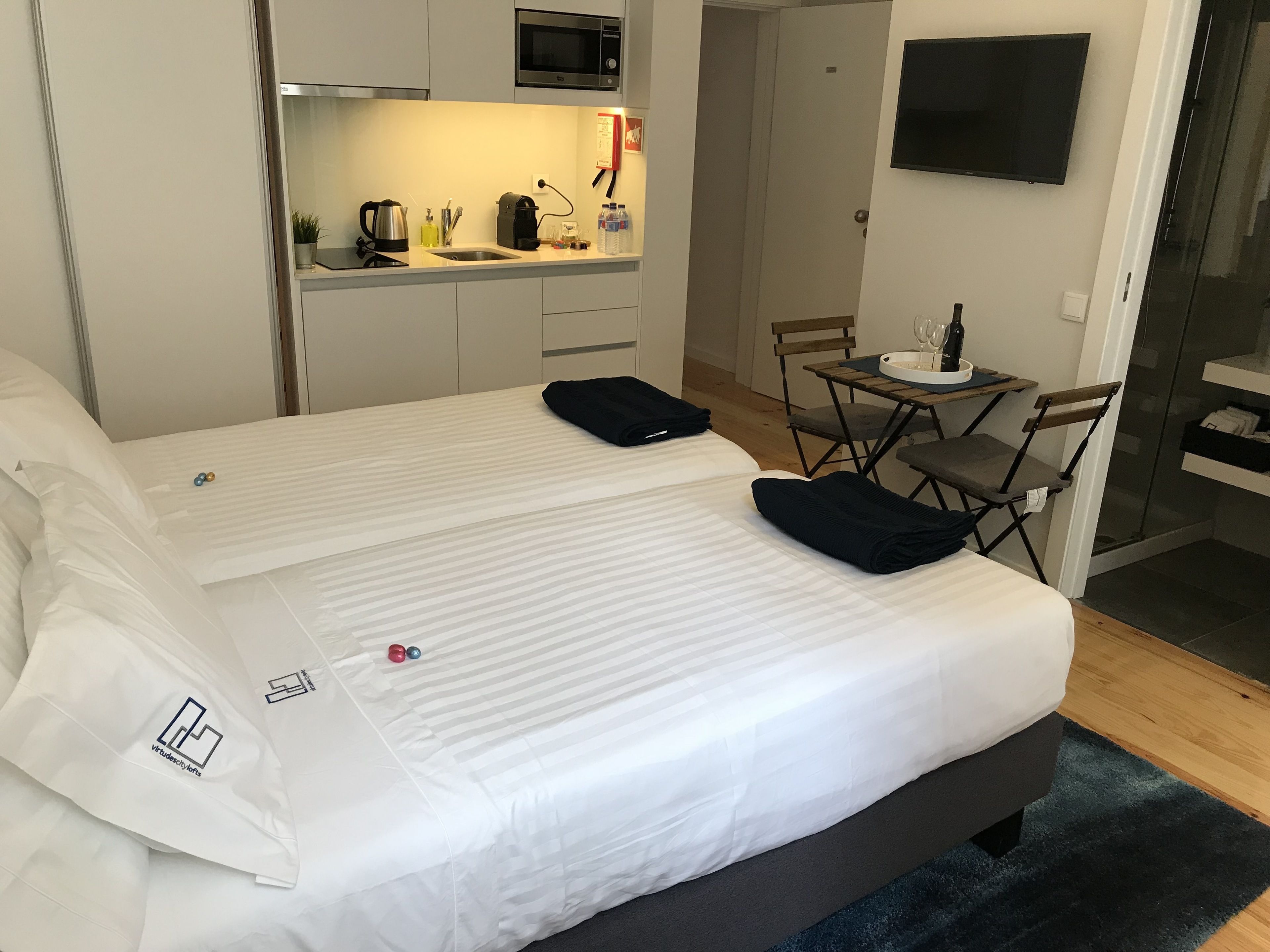 A hotel room with a large bed, a small kitchenette, a TV, and a shower area.