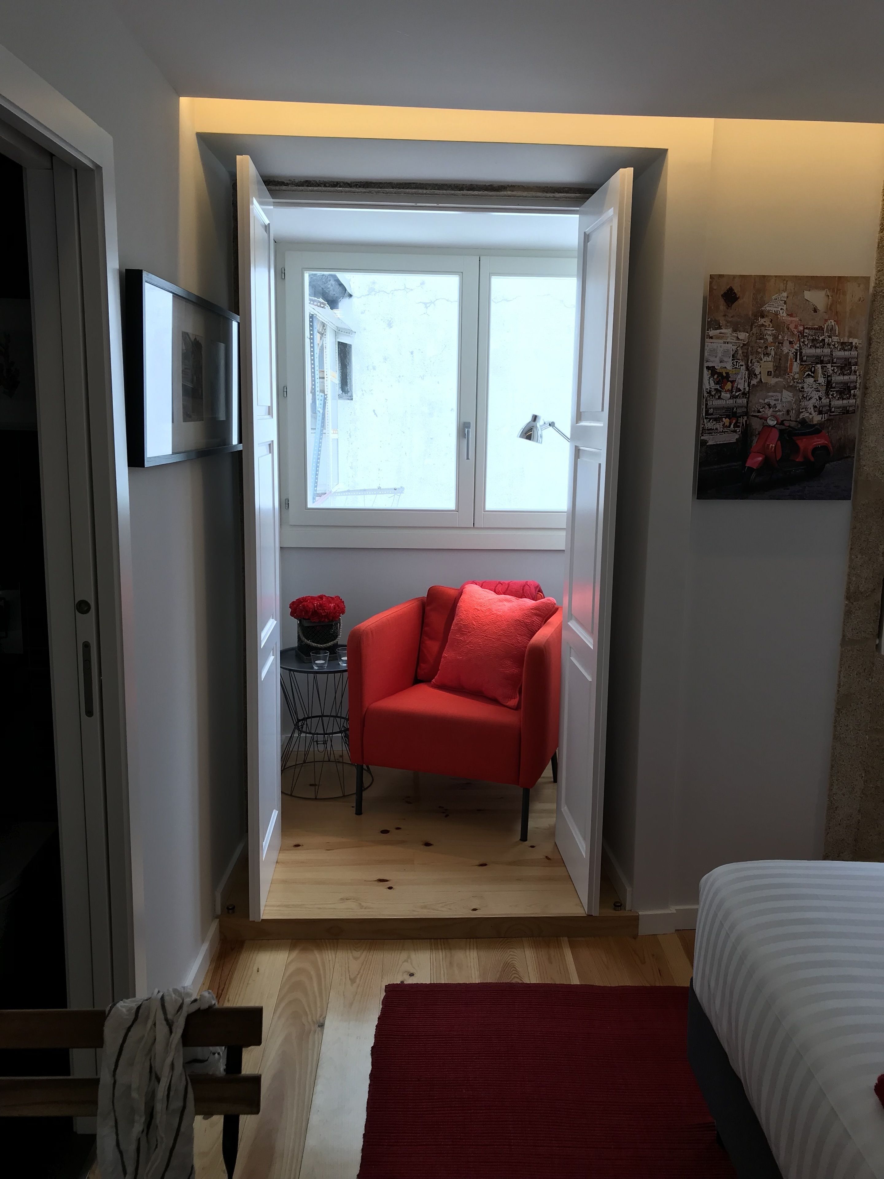 A compact bedroom with a red chair, a bed, and a small table with a vase.