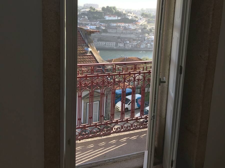 Vista de uma varanda com guarda-corpo de metal vermelho, com vista para um corpo de água e uma cidade com edifícios e uma ponte.