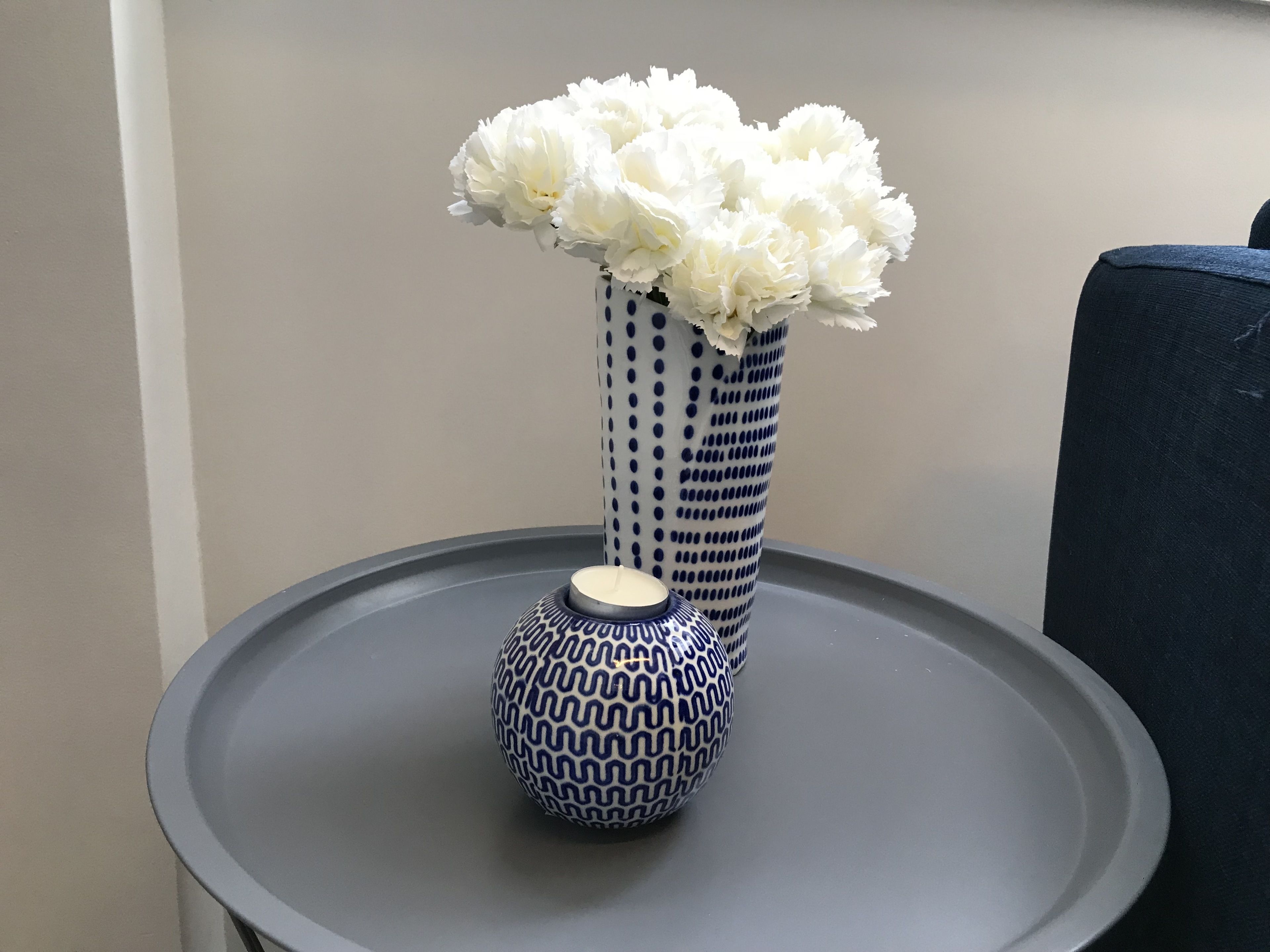 A blue and white patterned vase with a candle and white flowers on a round table.