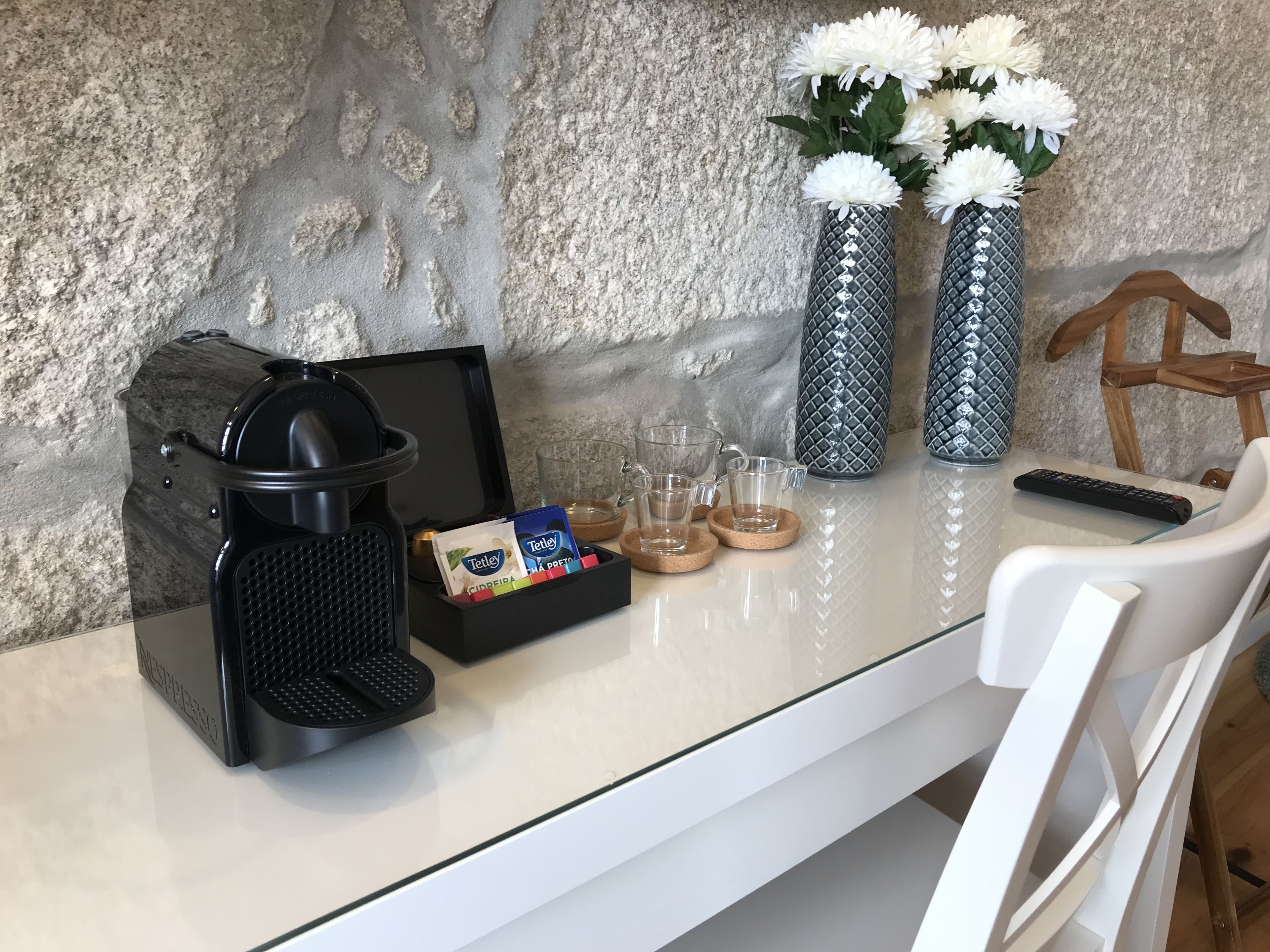 A coffee maker, two vases with white flowers, a remote control, and a tray with coffee pods and glasses on a table.