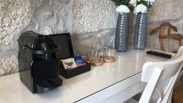 A coffee maker, two vases with white flowers, a remote control, and a tray with coffee pods and glasses on a table.