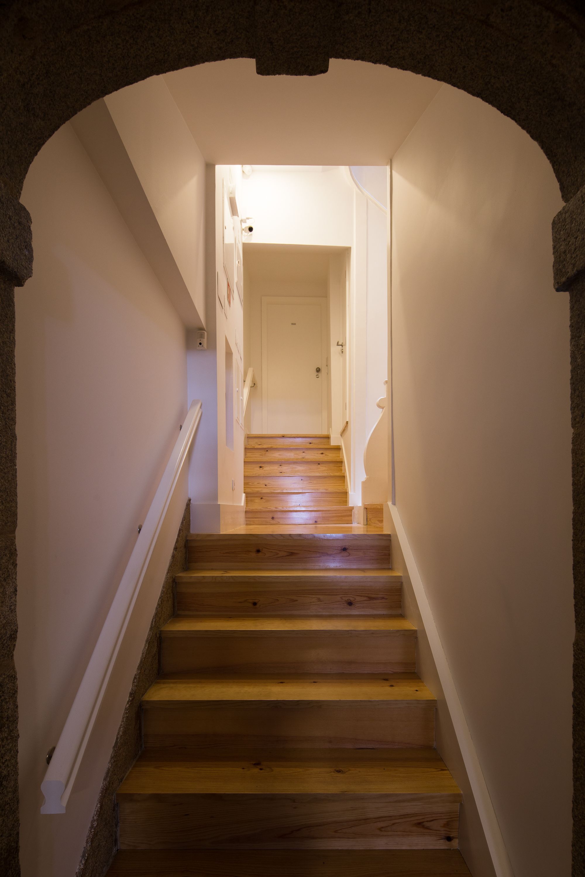 A wooden staircase with white walls and a white door at the top.