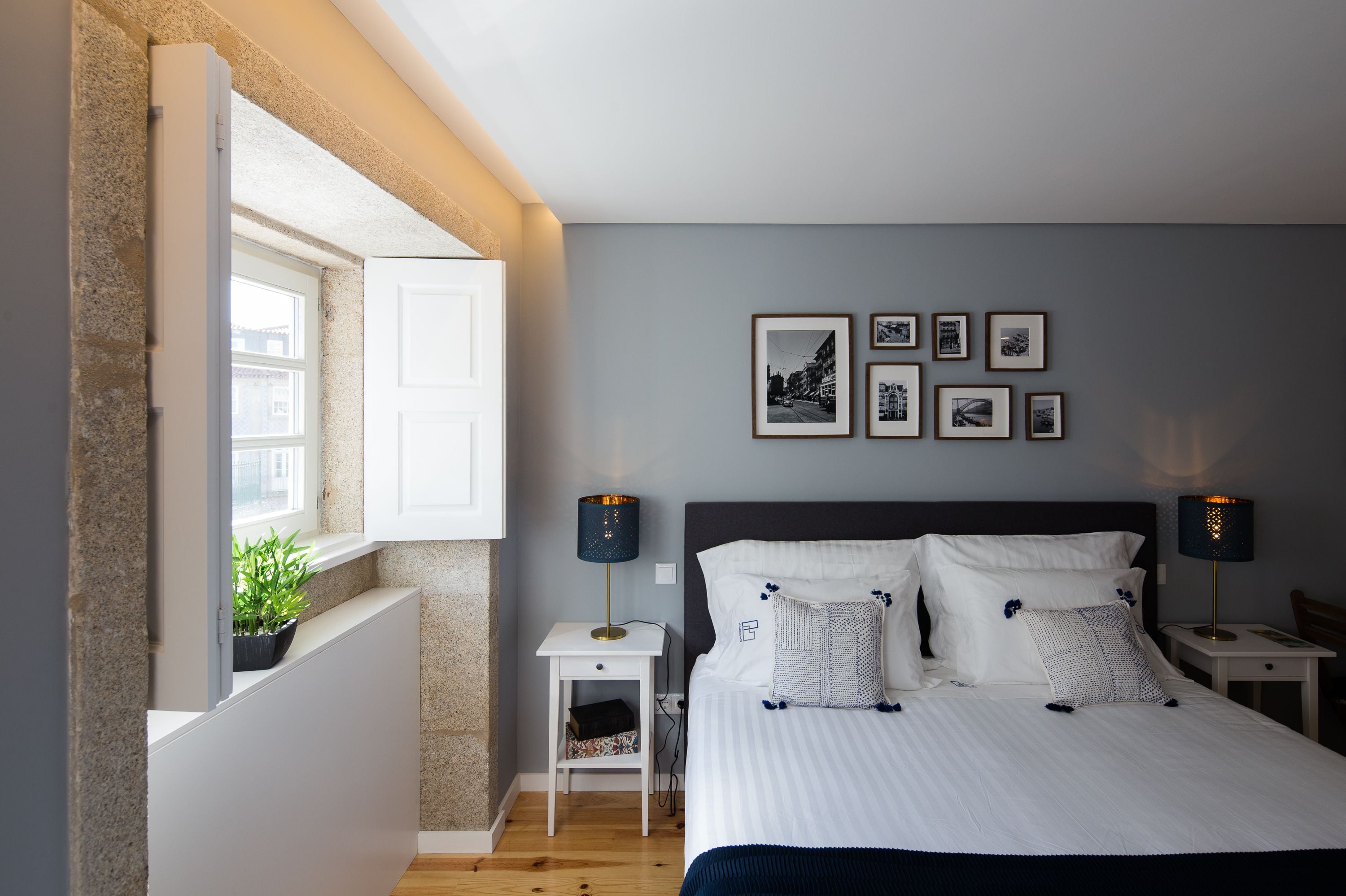 A bedroom with a bed, bedside tables, a window with a view, and framed pictures on the wall.