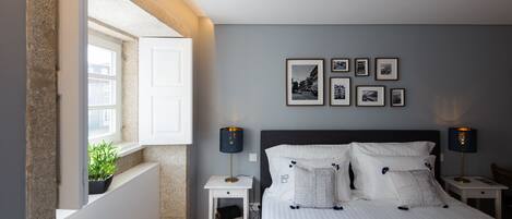 A bedroom with a bed, bedside tables, a window with a view, and framed pictures on the wall.