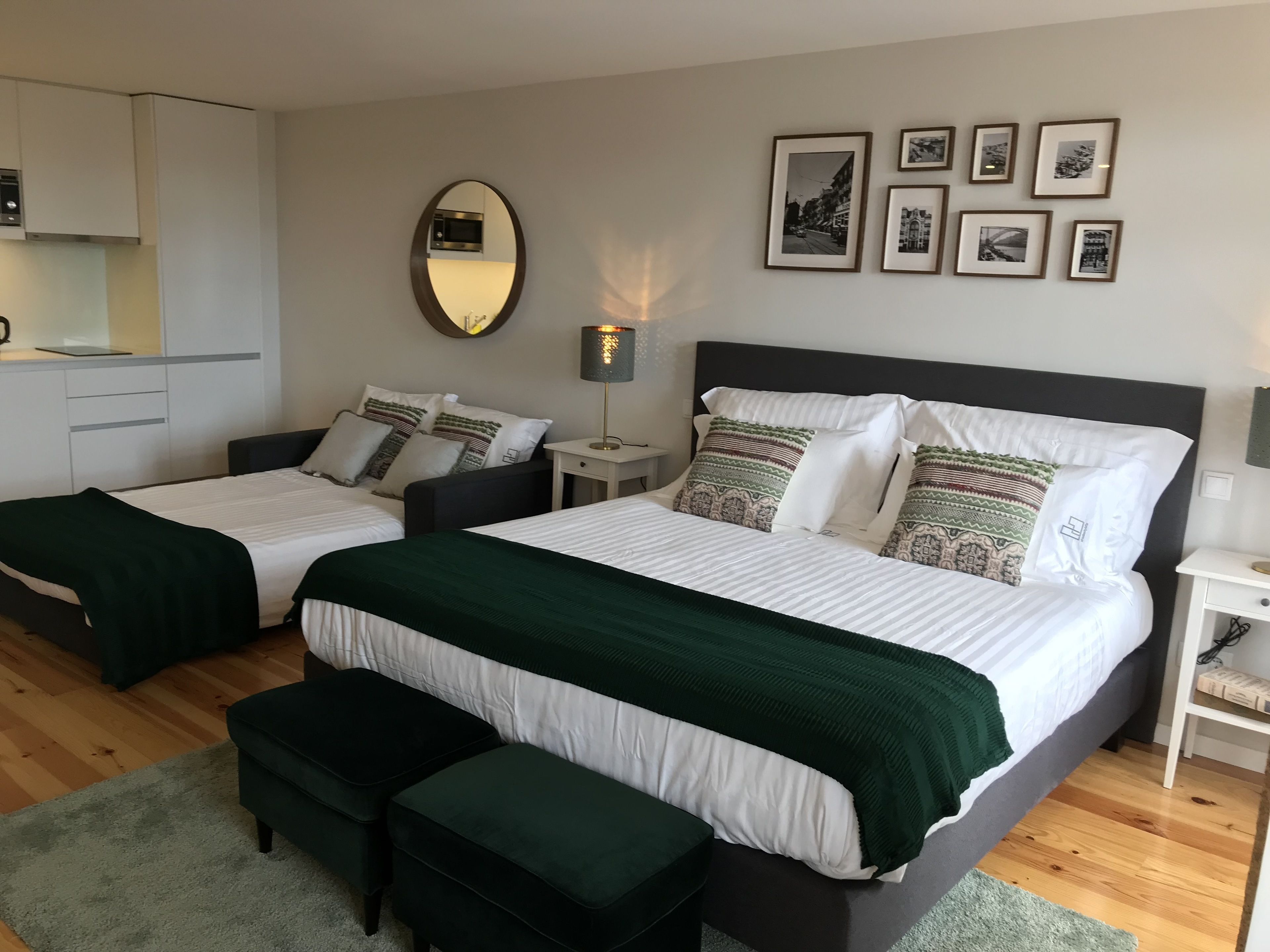 A hotel room with two beds, a small kitchenette, a mirror, and framed pictures on the wall.