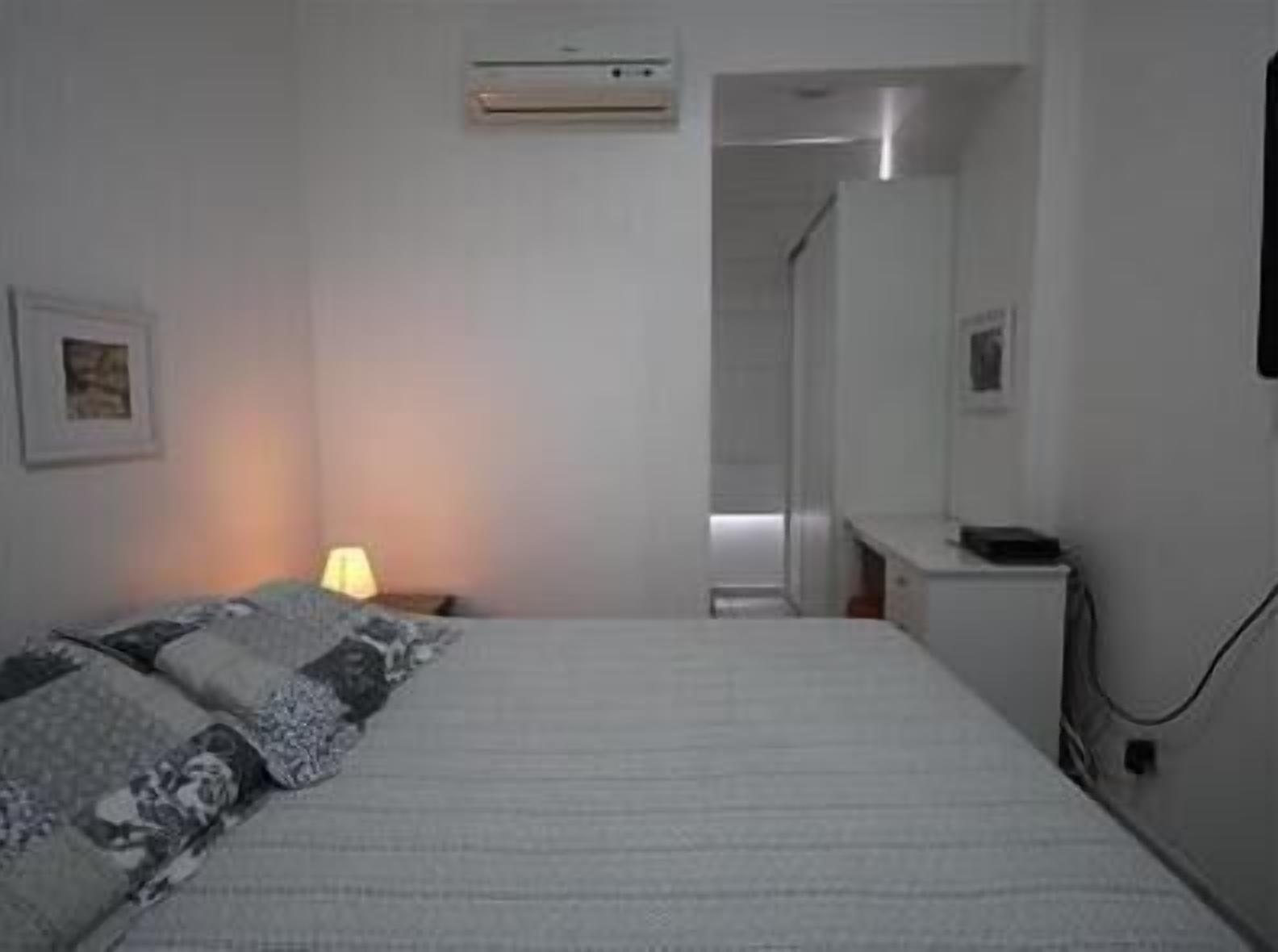 Une chambre à coucher comprenant un lit, une table de chevet, une lampe et un climatiseur fixé au mur.
