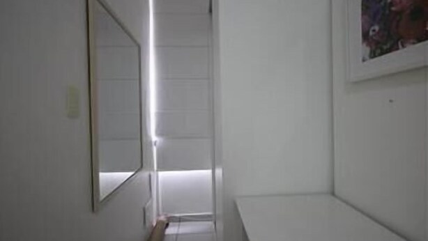 Ein schmaler Flur mit weißen Wänden, einer langen Leuchtstoffröhre und einem gerahmten Bild rechts.