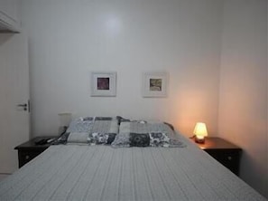 A bedroom with a bed, a nightstand, and two wall-mounted pictures.