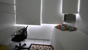 Ein kleiner, einfach eingerichteter Raum mit einem Bett, einem Stuhl und einem Schreibtisch.
