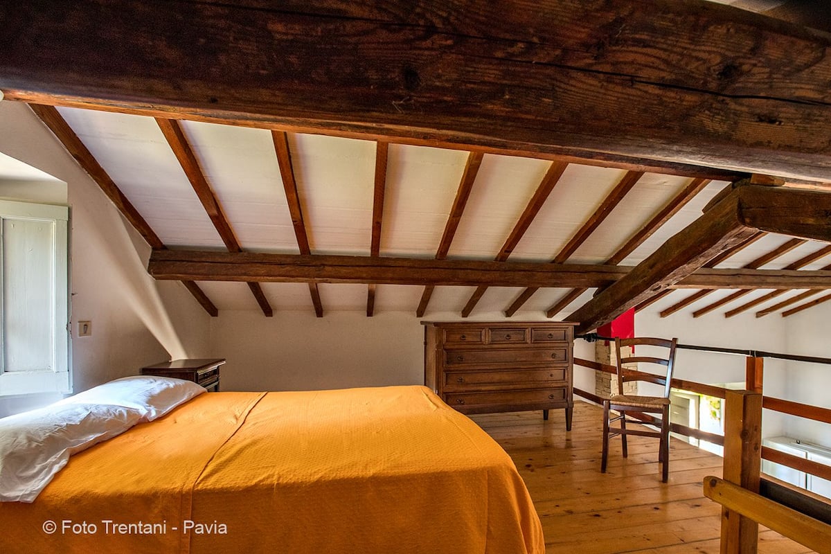 A bedroom with a wooden ceiling, a bed with an orange bedspread, a wooden dresser, and a chair.