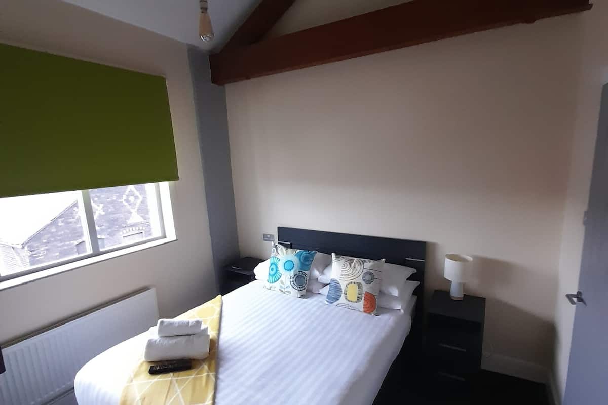 A bedroom with a bed, bedside tables, a window with blinds, and a radiator.