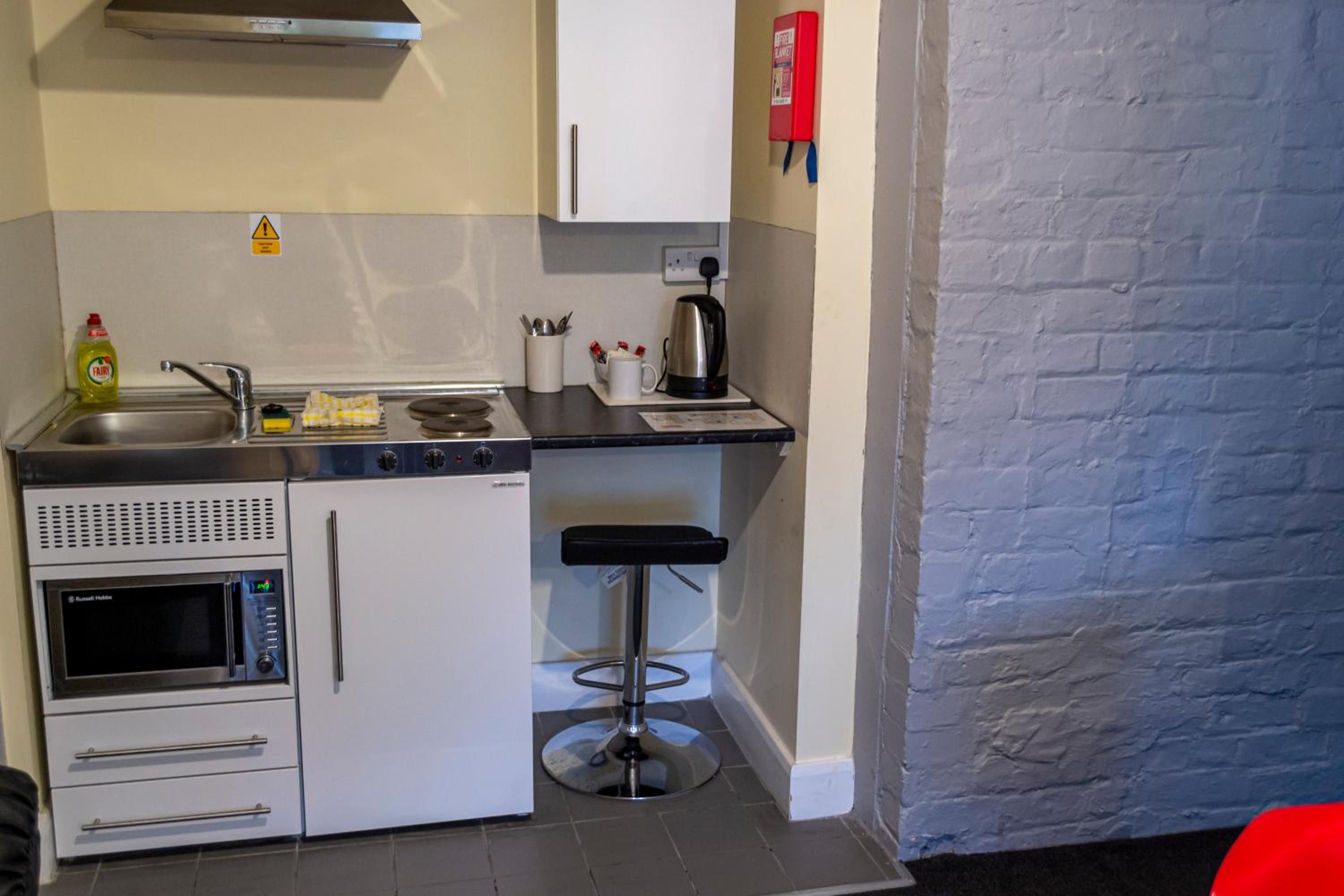 A compact kitchenette with a microwave, oven, sink, and a small bar stool.