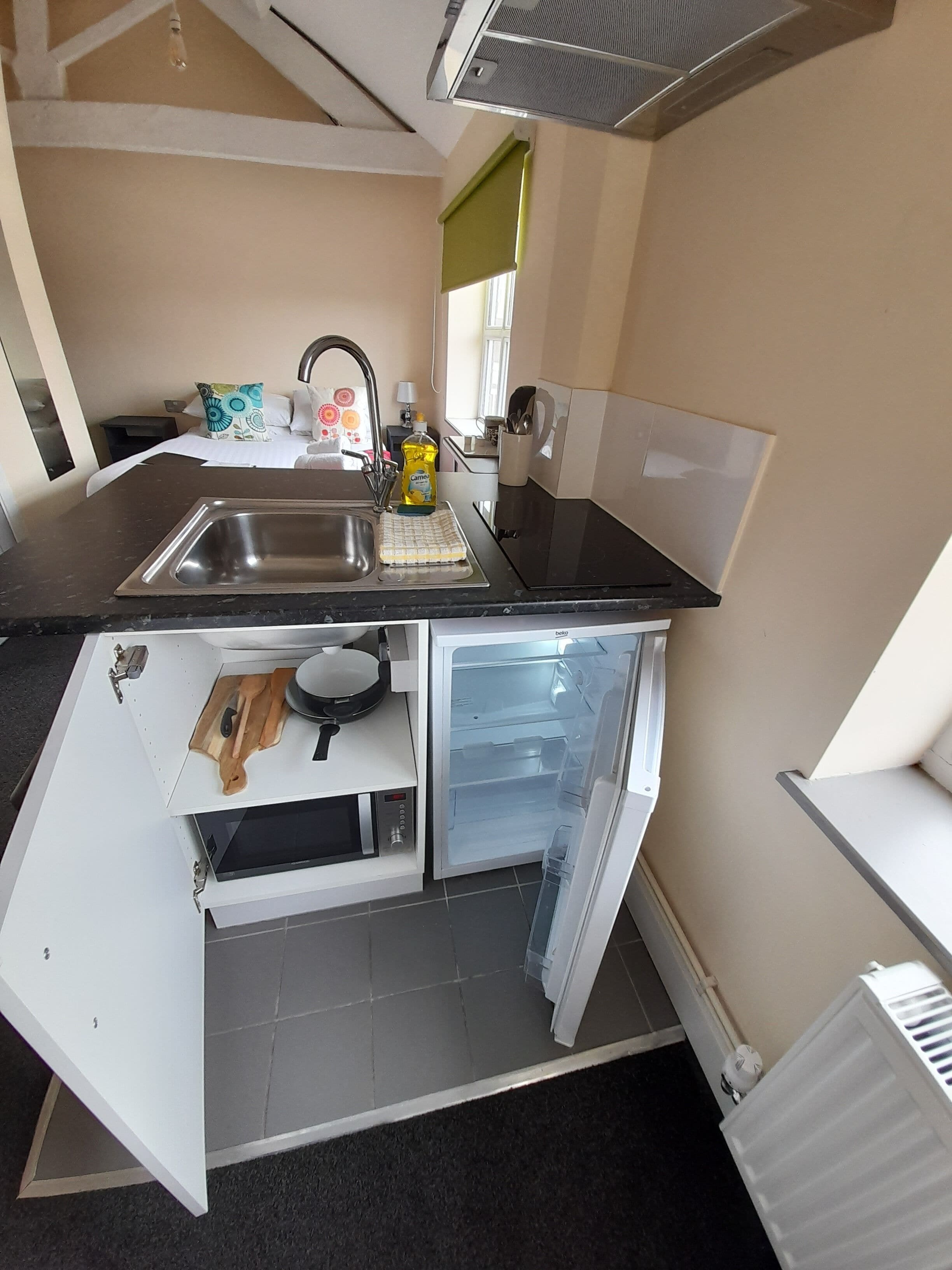 Una cocina compacta con lavamanos, microondas y refrigerador integrado.