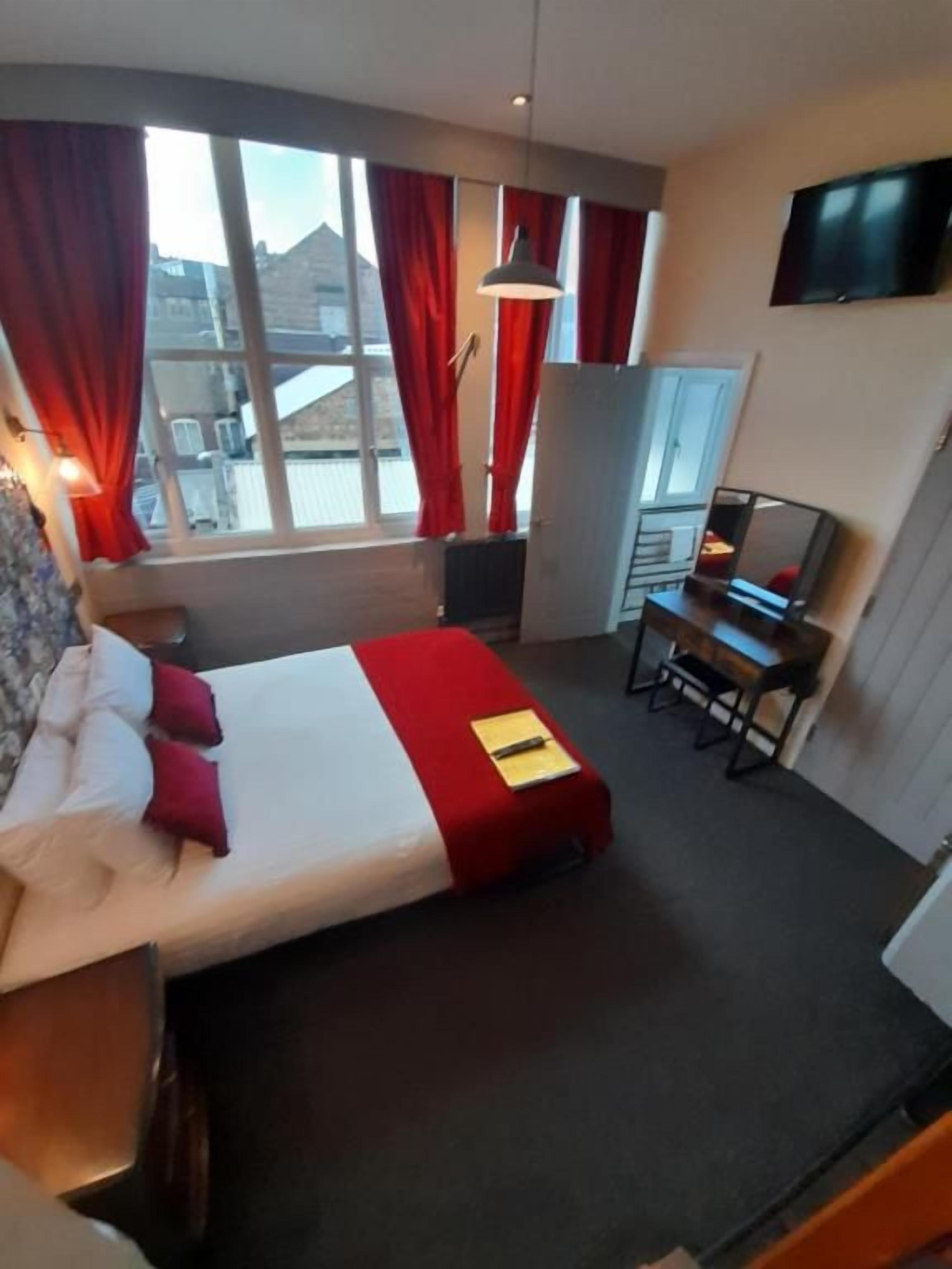 A hotel room with a bed, a desk, a chair, a TV, and a window with curtains.