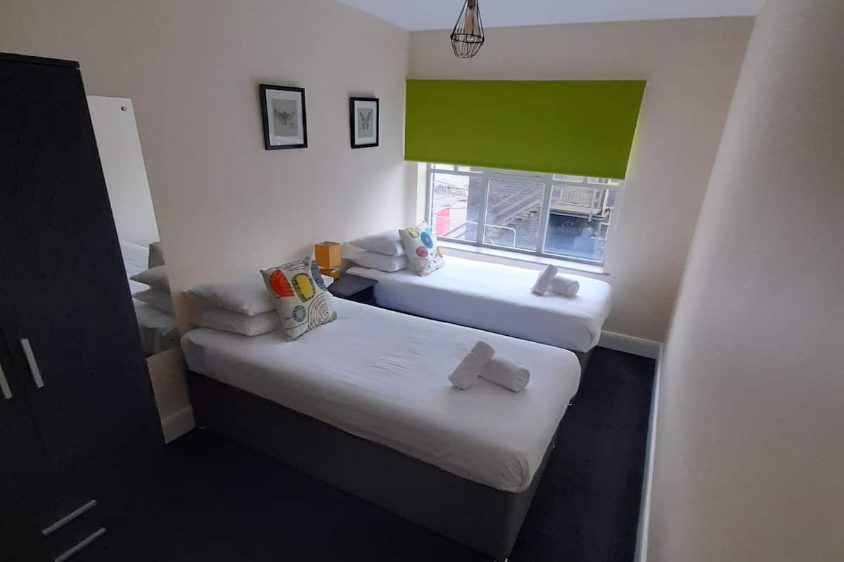 A modern hotel room with a large bed, a smaller bed, a window with a view of the street, and a green accent wall.
