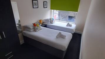 A modern hotel room with a large bed, a smaller bed, a window with a view of the street, and a green accent wall.