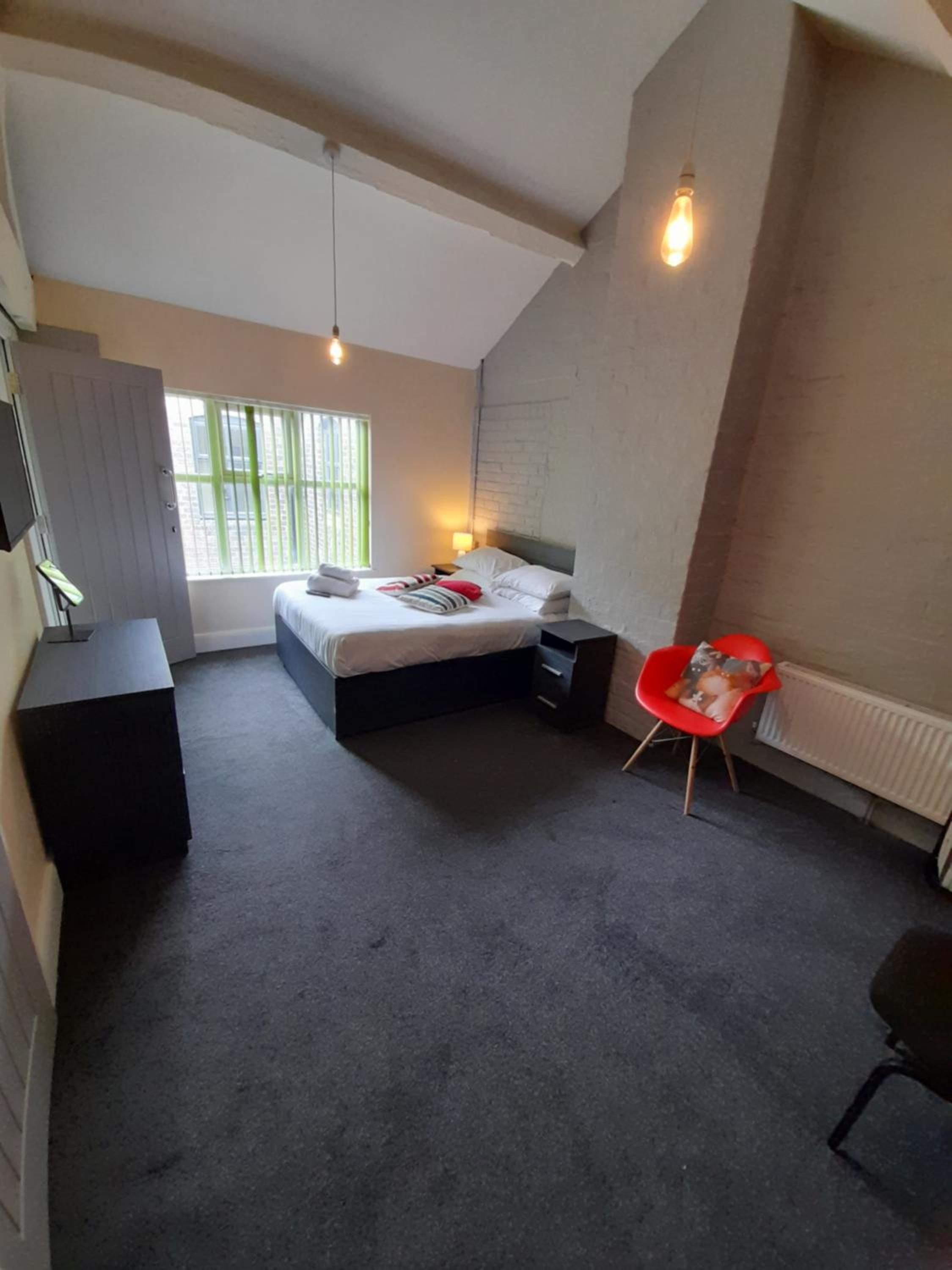 A bedroom with a bed, bedside table, chair, and a window with blinds.