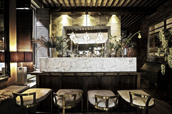A bar area with a marble countertop, hanging pendant lights, and three upholstered bar stools.