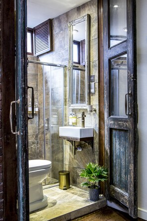 A bathroom with a marble wall, a white sink, a toilet, a potted plant, and a wooden door. - The Cow Hollow Hotel (Manchester)