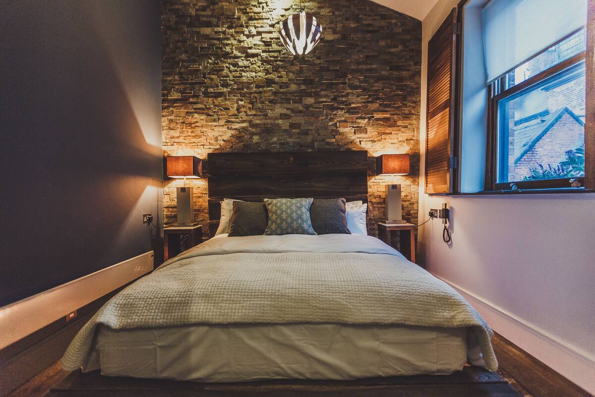 A bed with a headboard, two bedside lamps, and a view of a brick wall and window.