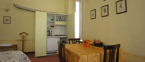 A room with a bed, a dining table with chairs, a kitchen area, and a window.
