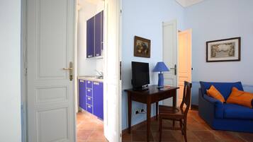 A living room with a blue sofa, a wooden table with a TV, and a kitchen area with blue cabinets.