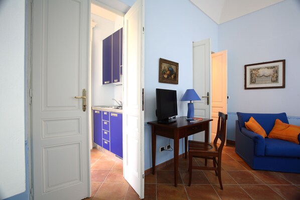 Una sala de estar con un sofá azul, una mesa de madera con un televisor y una zona de cocina con armarios azules.