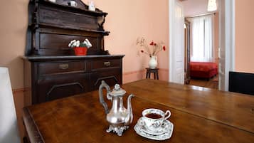 Una mesa de comedor de madera con una tetera de plata y una taza, un florero rojo y un aparador de madera con objetos decorativos.