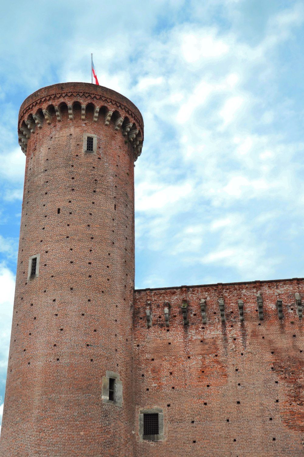 A brick tower with a flag on top, set against a partly cloudy sky.