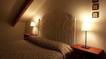 Ein Schlafzimmer mit schräg versiegelter Decke, einem Bett mit blumigem Bettbezug, zwei Nachttischen mit Lampen und drei gerahmten Bildern an der Wand.