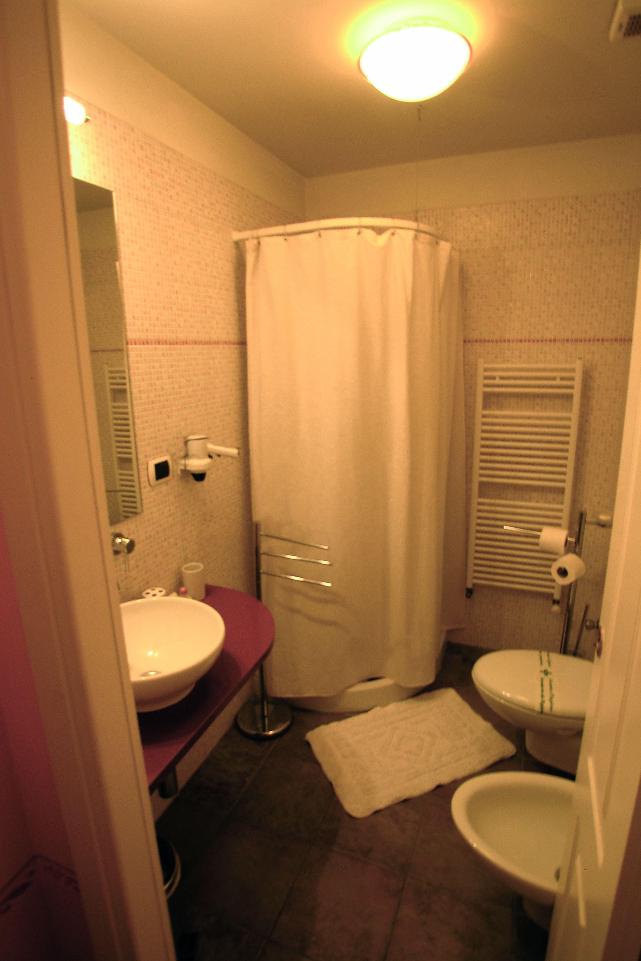 A small bathroom with a shower curtain, a sink, a toilet, and a bidet.