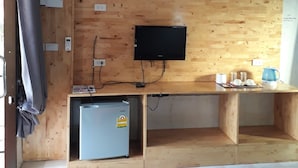 A room with a wooden wall, a flat-screen TV mounted above a wooden desk, a small refrigerator, and a kettle on the desk. - Poopreaw Resort (Koh Lan)