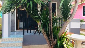 A small garden area with a palm tree, a concrete table, and a stone pathway leading to a building with a blue and white facade. - Poopreaw Resort (Koh Lan)