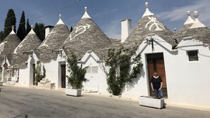 A row of white buildings with conical roofs, a paved street, and a clear blue sky. - Villa Aurora B&B (Bari)
