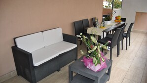 A modern outdoor seating area with a sofa, dining table, chairs, and a small table with a flower arrangement. - Villa Aurora B&B (Bari)