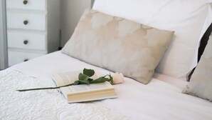 A neatly made bed with a white pillow, a book, and a rose. - Villa Aurora B&B (Bari)