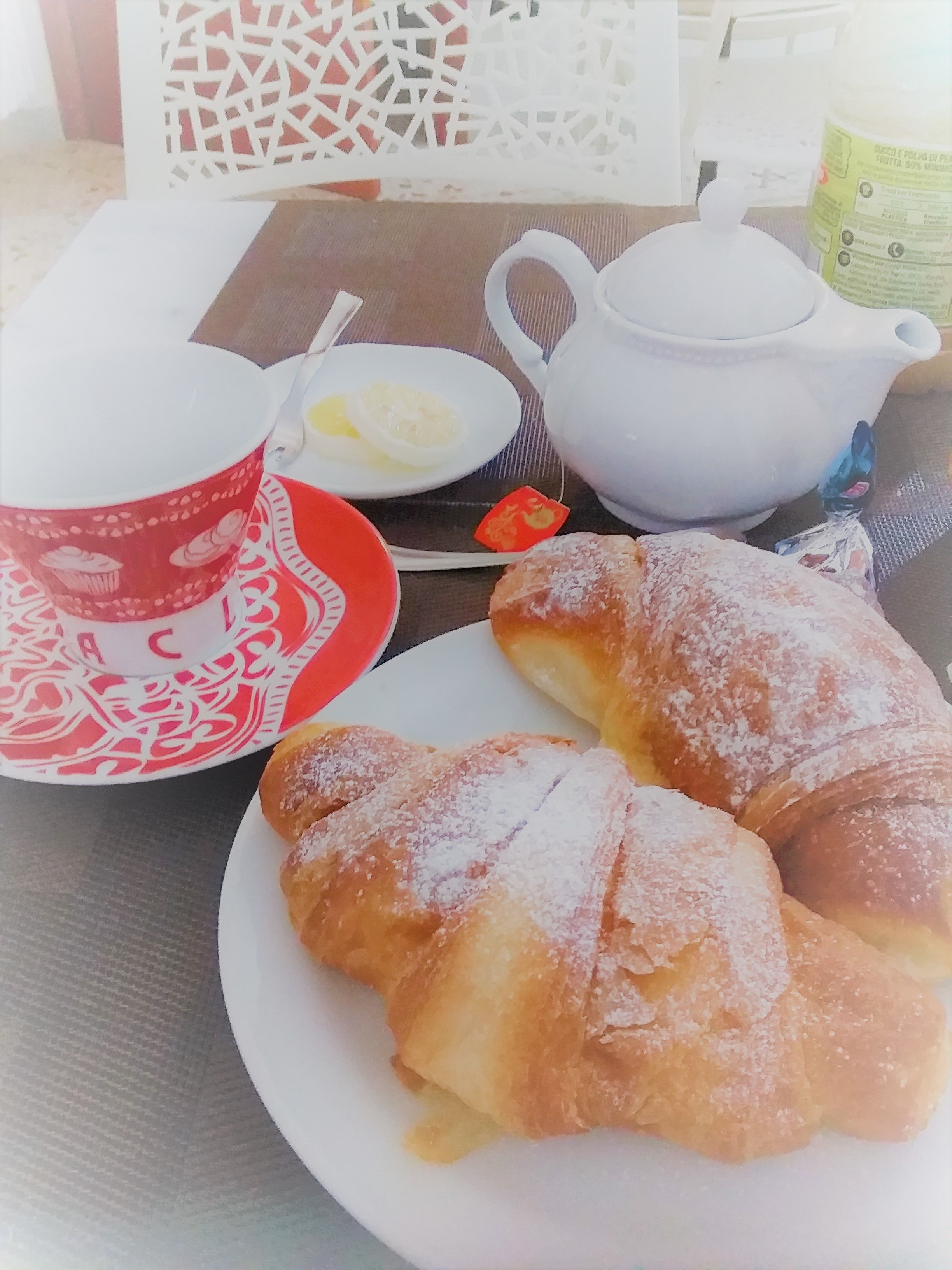 Uma mesa com um bule, uma xícara, um prato com doces e um pequeno recipiente com manteiga.