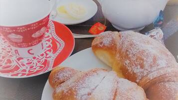 Uma mesa com um bule, uma xícara, um prato com doces e um pequeno recipiente com manteiga.