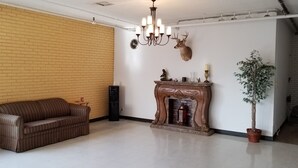 A living room with a brick wall, a wooden fireplace, a mounted deer head, a chandelier, a sofa, and a potted plant. - Americas Premier Inn (Sweetwater)