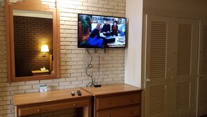 A hotel room with a brick wall, a wooden desk, a mirror, a television mounted on the wall, and a set of closets. - Americas Premier Inn (Sweetwater)