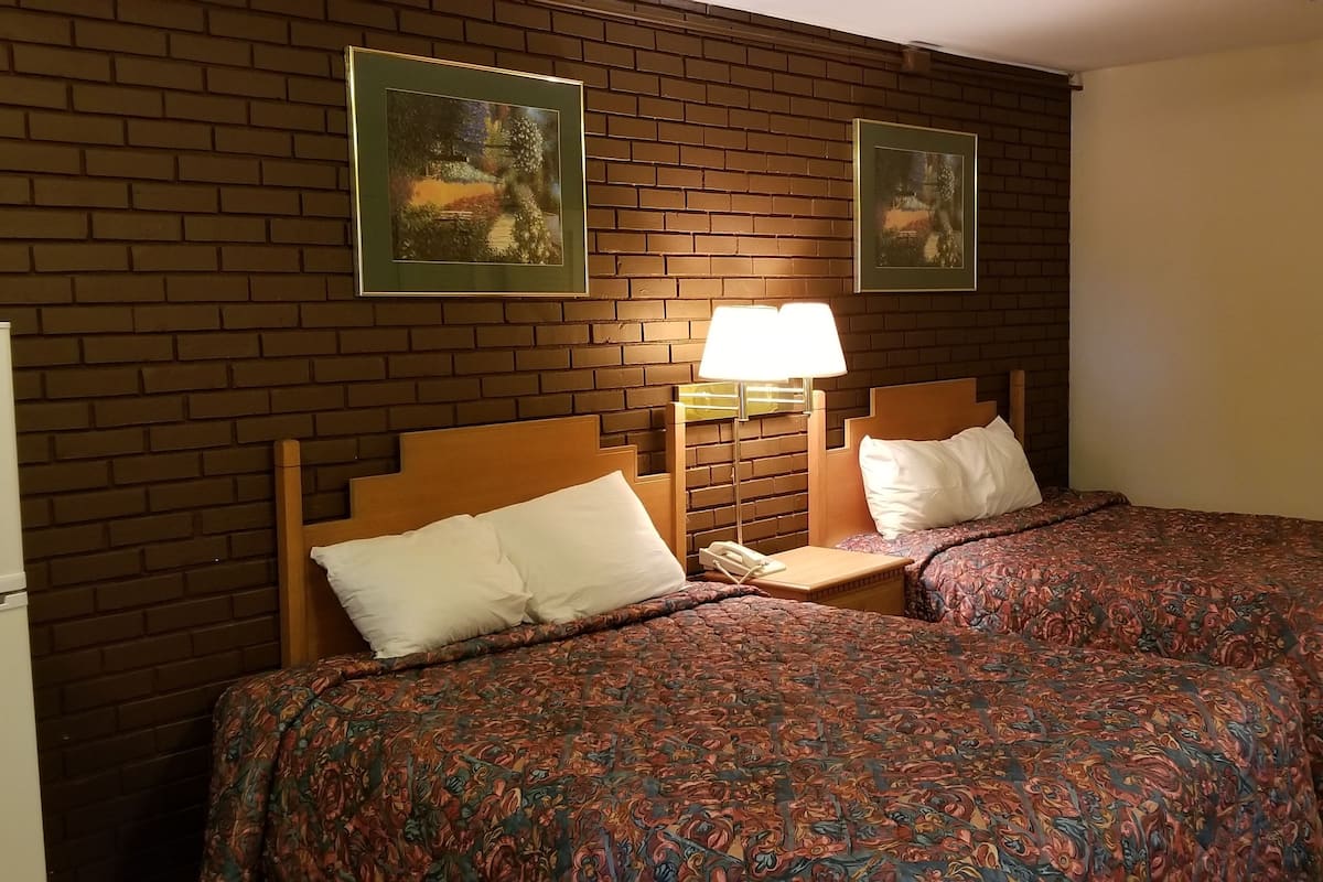 Quarto de hotel com duas camas, uma mesa de cabeceira com abajur, um frigorífico e duas molduras na parede.