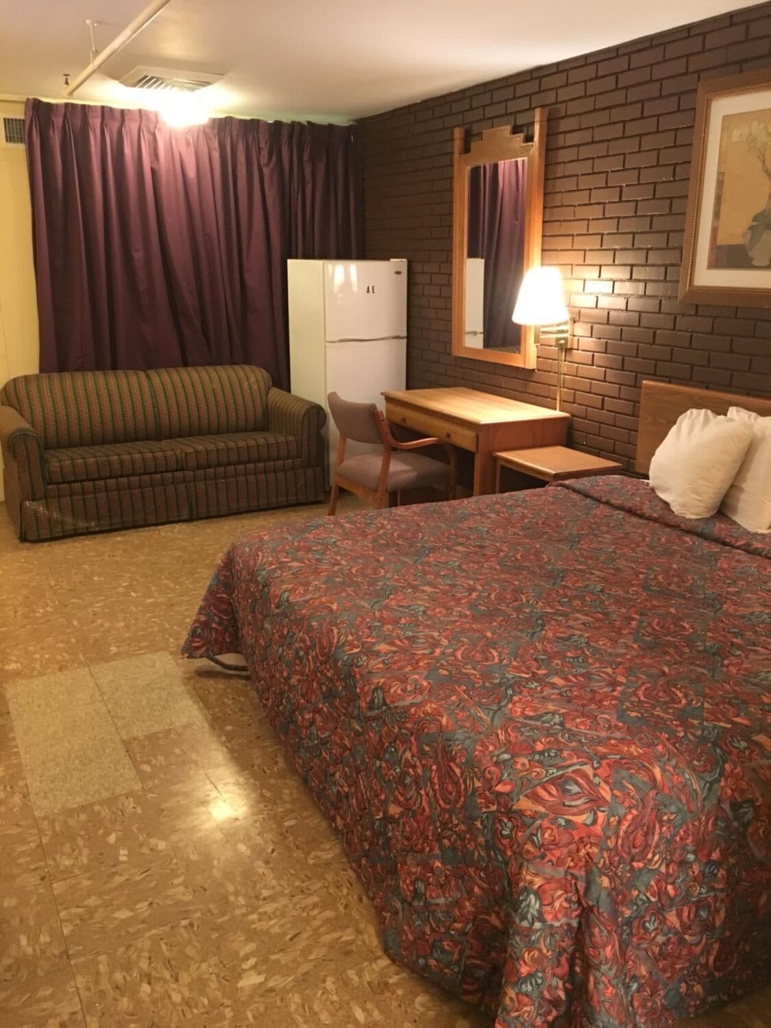 A room with a bed, a sofa, a desk, and a refrigerator.