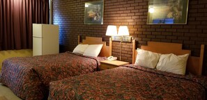 A hotel room with two beds, a nightstand with a lamp, a refrigerator, and a brick wall with framed pictures. - Americas Premier Inn (Sweetwater)