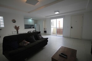 Una sala de estar con un sofá oscuro, una mesita de centro y una cocina al fondo.