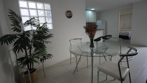 Een moderne eetruimte met een glazen tafel, metalen stoelen, een potplant en een raam met jaloezieën.