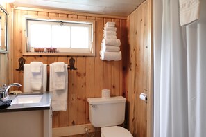 A wooden-paneled bathroom with a sink, two towels, a toilet, and a window.