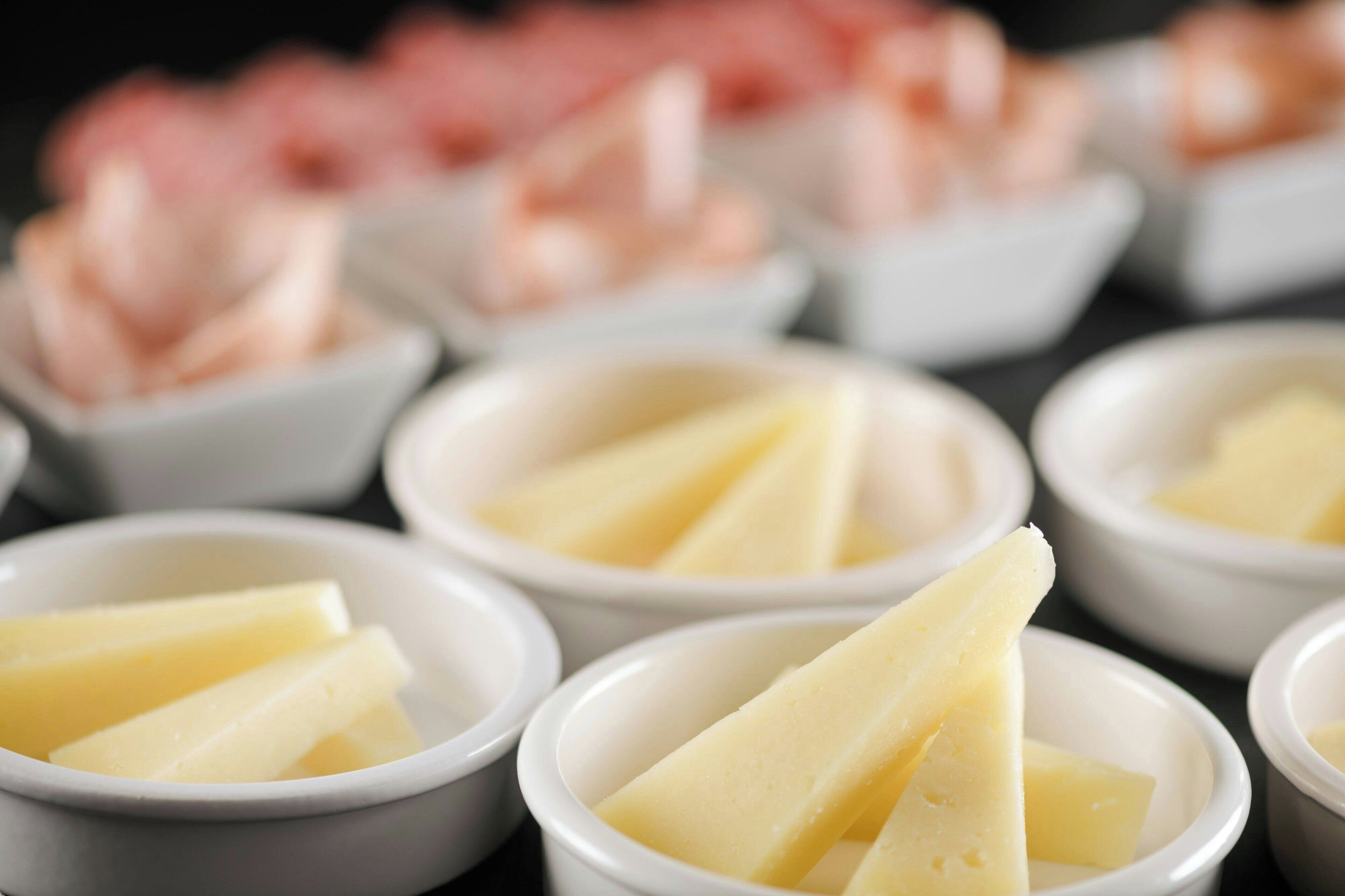 Varios cuencos pequeños blancos con tajadas de queso amarillo y camarones rosados.