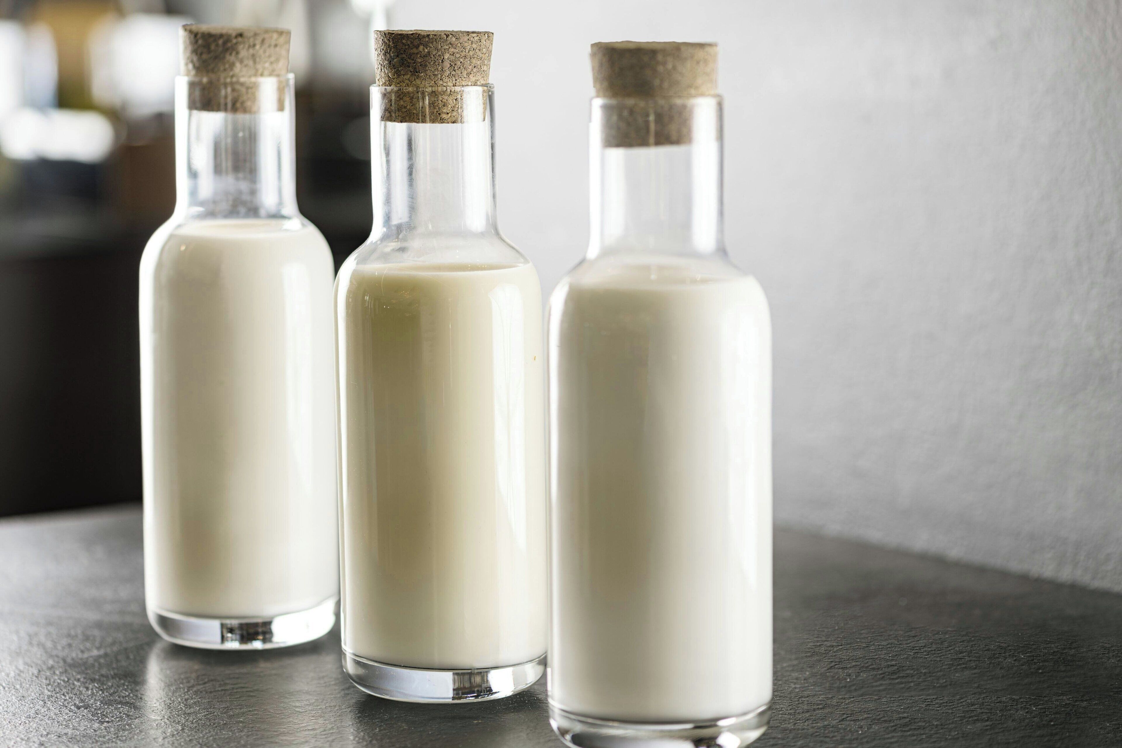 Three glass bottles with cork stoppers containing a white liquid, likely milk, on a dark surface.